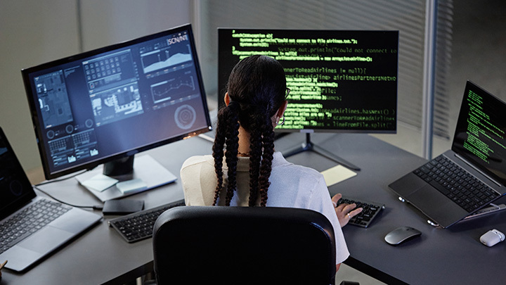 Woman sat at desk with three computer screens showing data