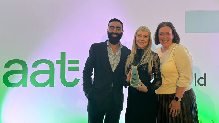 Three people holding AAT award in front of AAT logo