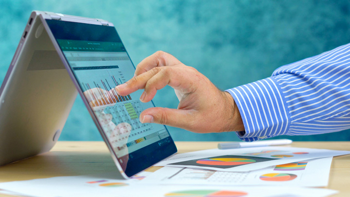 Man's hand touching laptop screen with Excel spreadsheet on it