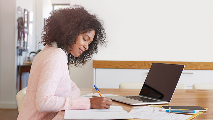 Woman writing with pen in front of laptop