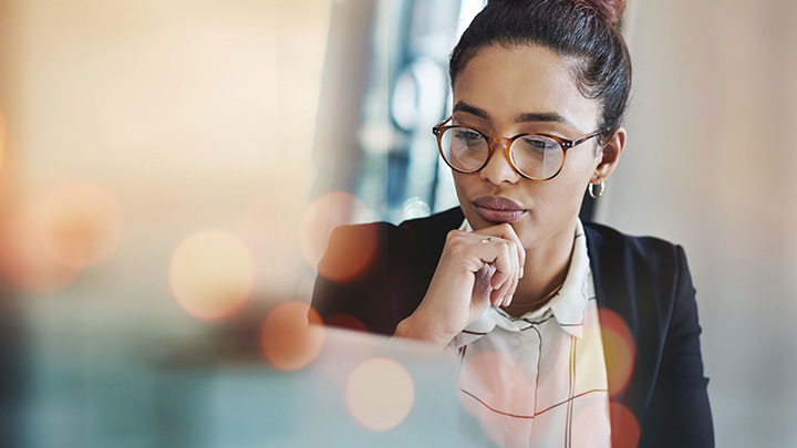 Professional woman wearing glasses thoughtfully looking down at a screen.