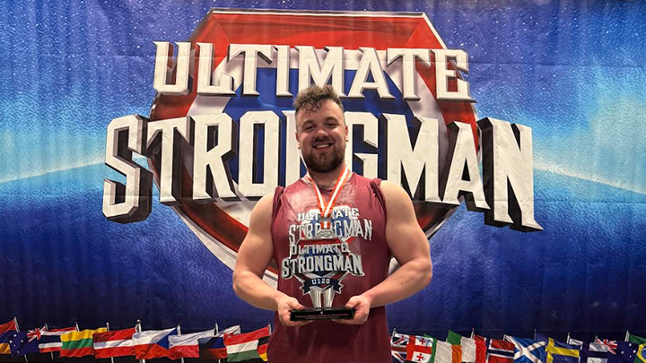 Luke Ogbourn with trophy in front of Ultimate Strongman banner