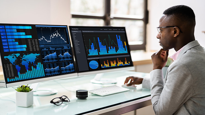 Man looking at computer screens with data graphs on them