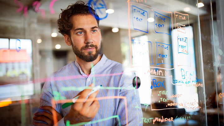 Man looking and writing on a clear version of a whiteboard