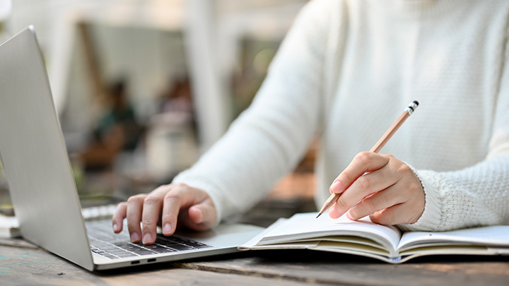 Woman writing on notepad whilst typing on laptop