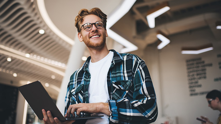Young professional smiling while using a laptop in a modern office during the early stages of professional study and work.