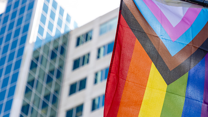 A rainbow pride flag waving in front of a modern building.