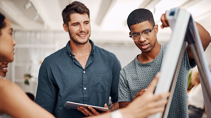 A group of young professionals collaborating around a whiteboard in a modern office, representing workplace skills and teamwork.
