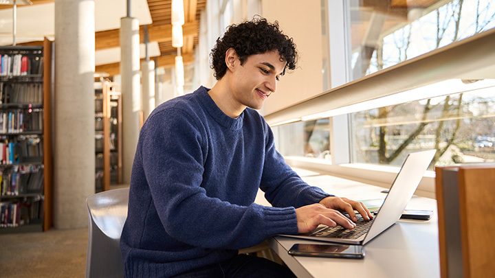 Young man in university library, working on laptop