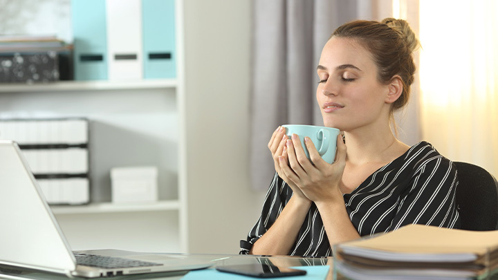 Woman at desk, holding mug, and closed eyes
