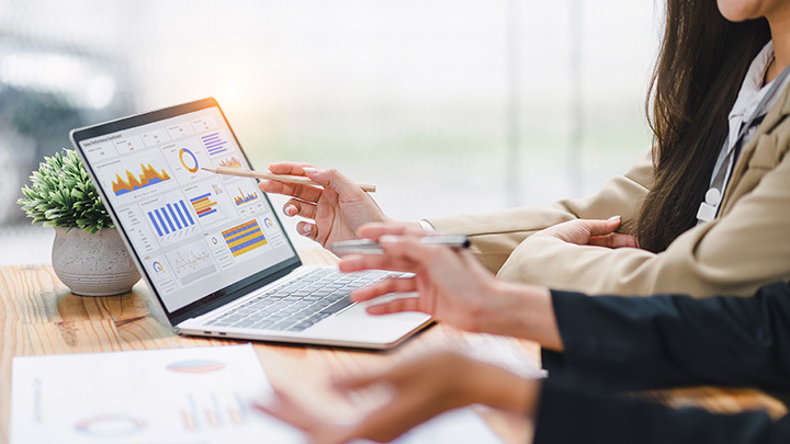 Two colleagues sat at a table interpreting and analysing data including graphs and pie charts