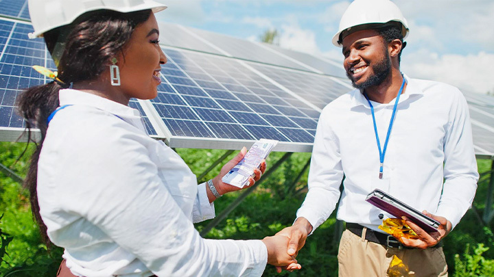Man and woman shaking hands in front of solar panels
