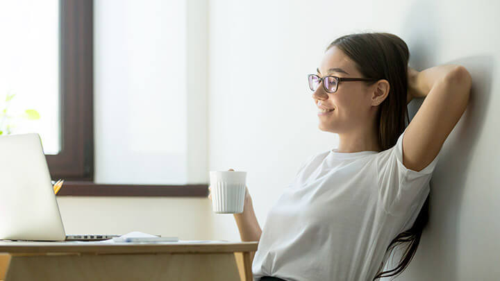 Female student smiling and holding a mug whilst watching a laptop