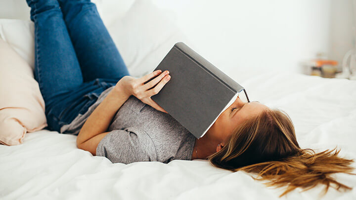 Student lying on a bed with head in a book