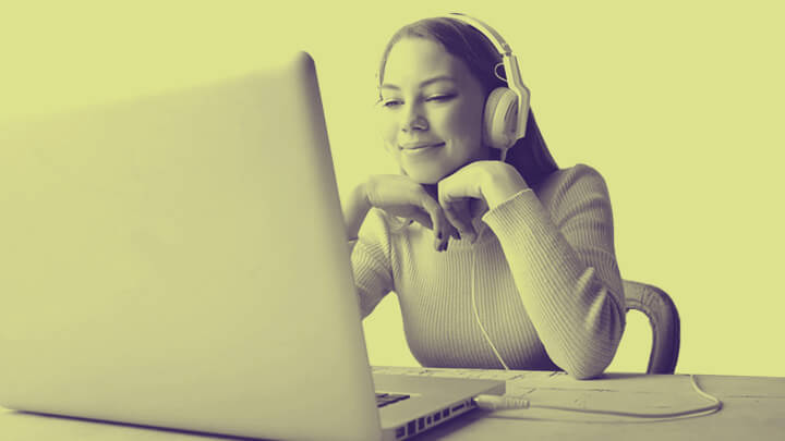 Woman with headphones on, smiling at laptop
