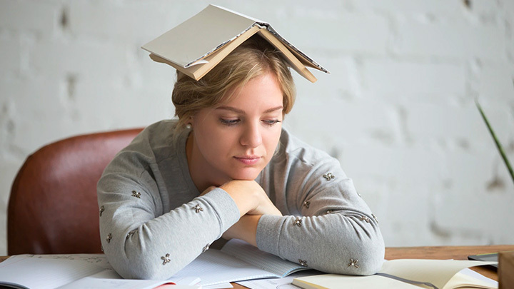 Woman leaning on desk with book on her head
