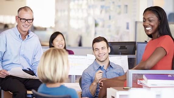Two men and three women in an office talking and smiling.