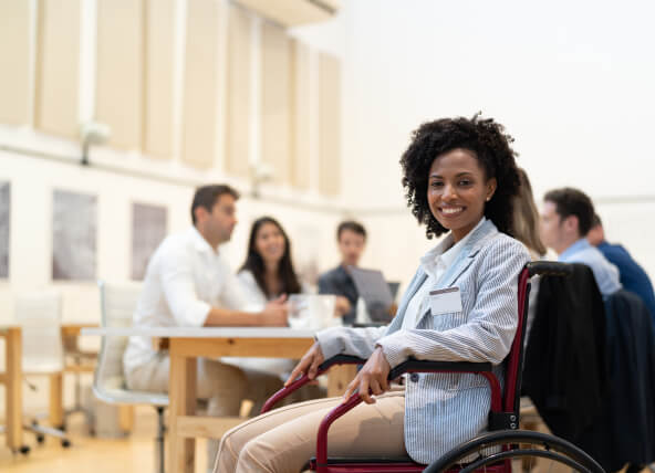 A woman in a wheelchair with people sat around a desk behind