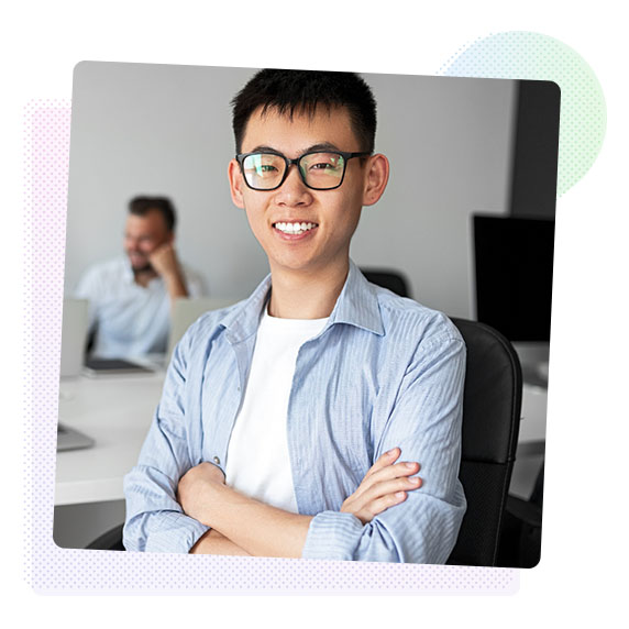A young man wearing glasses and a blue shirt smiles warmly at the camera