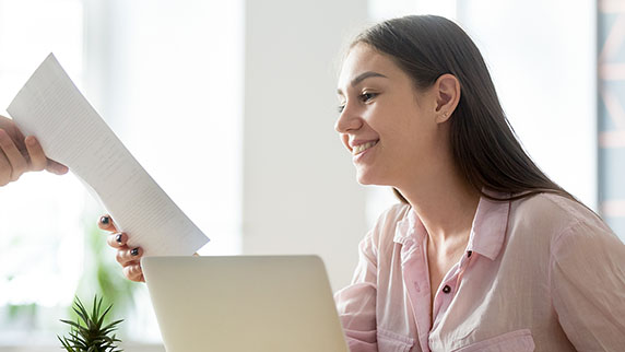 A woman sitting at a desk, holding a piece of paper, appears focused and engaged in her work