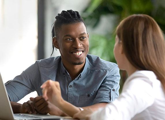 A man and a woman talking in front of an open laptop.