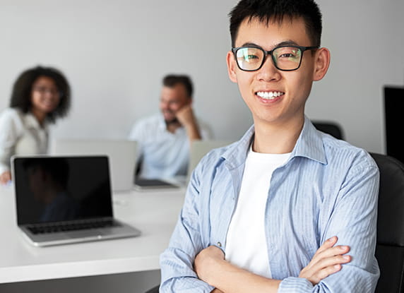 A man smiling with a laptop behind him.