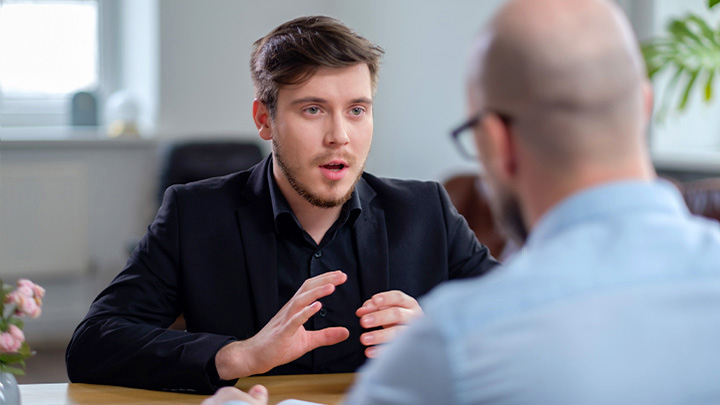 Two men sitting across a table from each other talking.