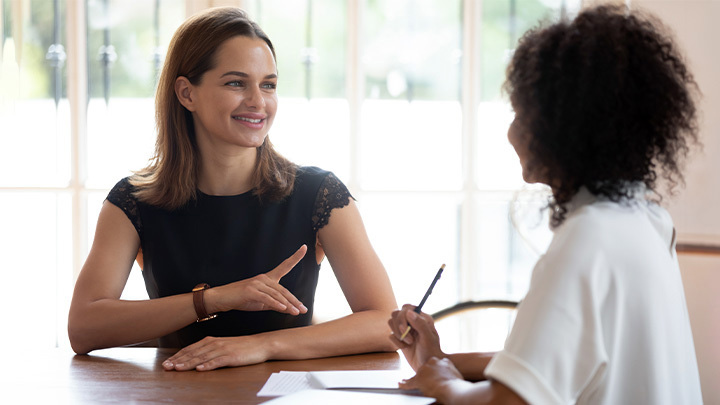 Two women sitting across a table from each other talking.