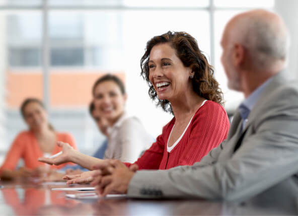 A lady sitting at a meeting table and smiling with other people around the table