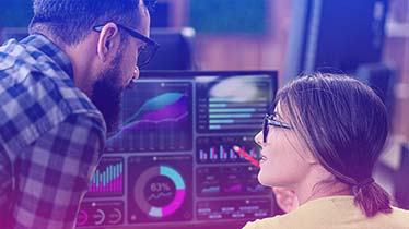 A man and a woman, both wearing glasses, looking at screens with data graphs