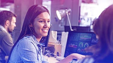 A women with data charts on a monitor in front of her looking at a colleague
