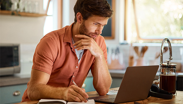 Man looking at a laptop and writing in a notebook