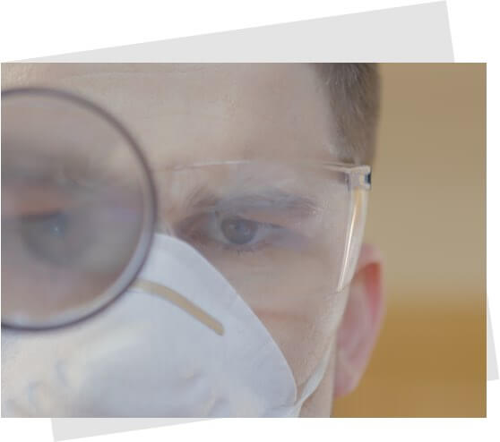 A man wearing a dust mask using a magnifying glass