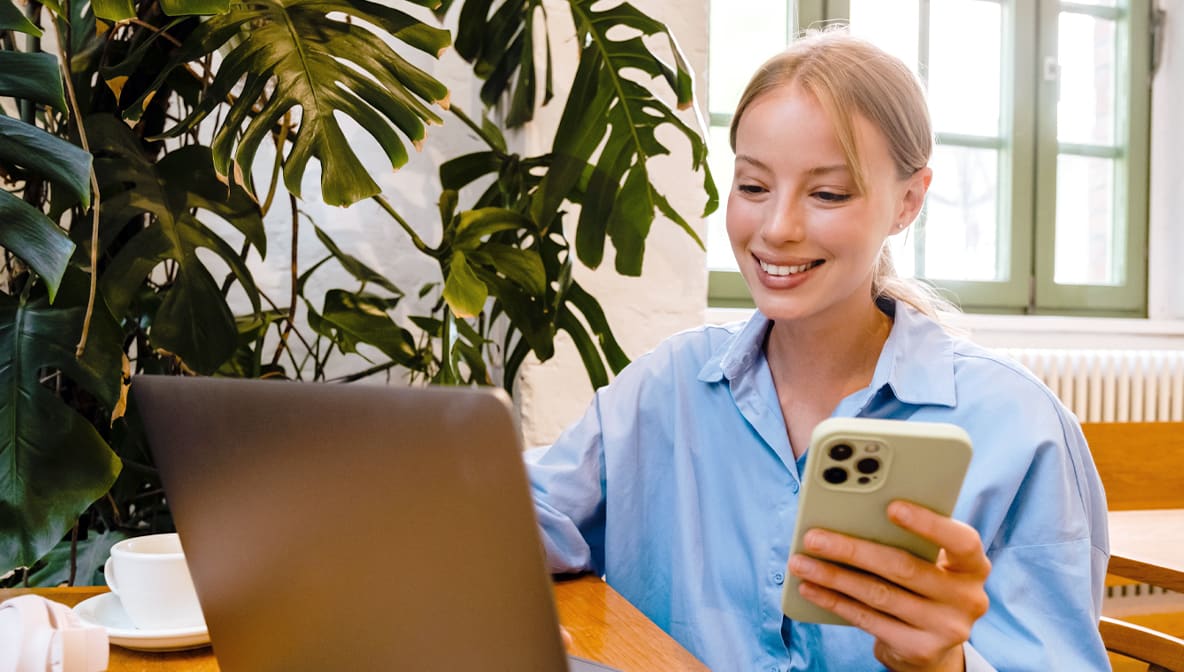 Woman holding a mobile phone looking at a laptop screen