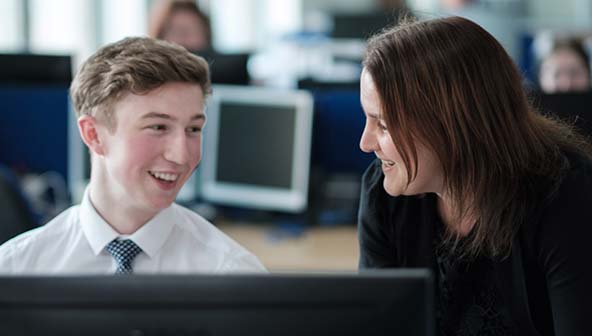 A man in a shirt and tie sitting down at a desk talking to a woman