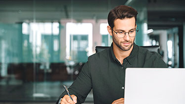 A man holding a pen looking at a laptop