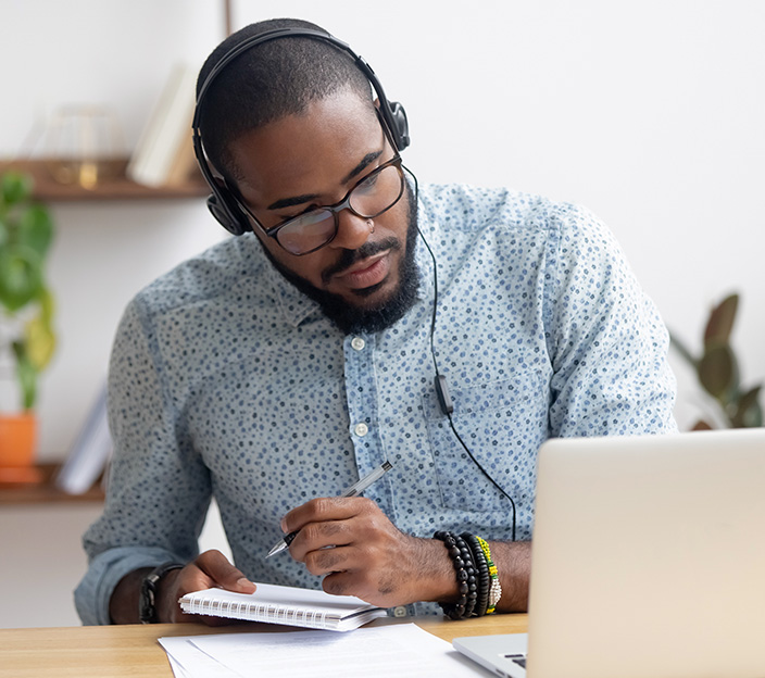 A man watching a video on a laptop and making notes