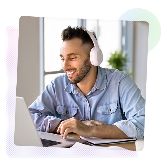 A man wearing headphones, smiling and working on a laptop.