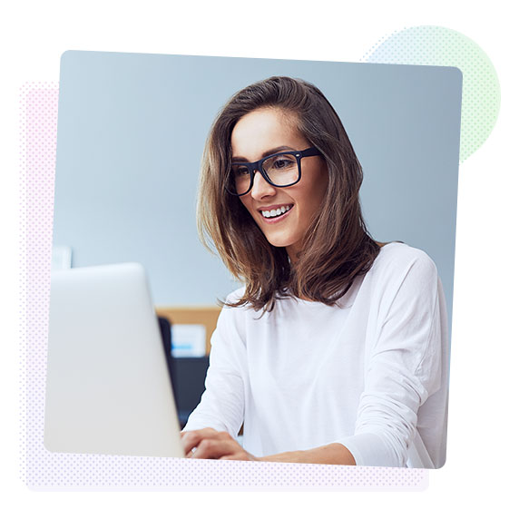 A woman wearing glasses smiles while working on her laptop