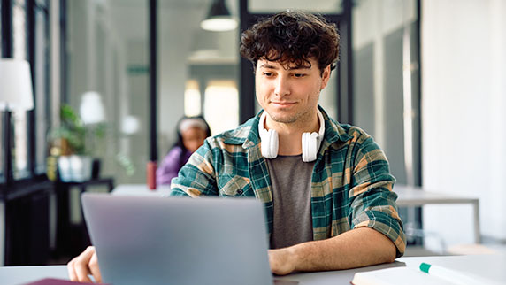 Man with headphones around his neck working on a laptop