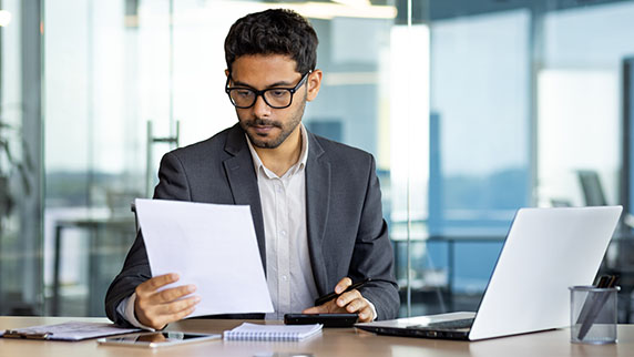 Man sat at a desk reading a sheet of paper