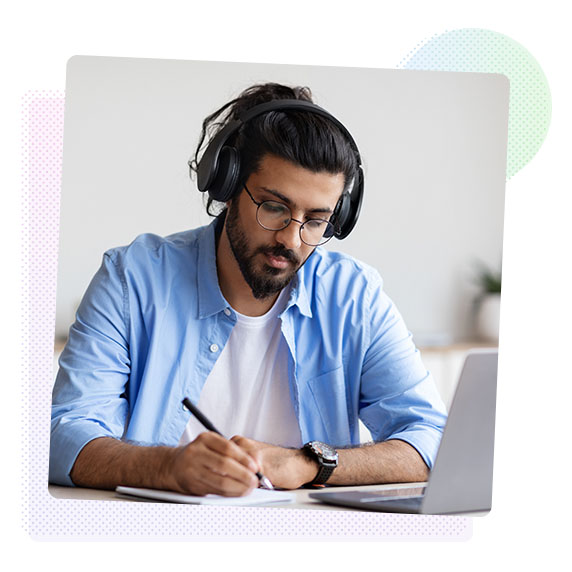 Man wearing headphones using a laptop and making notes
