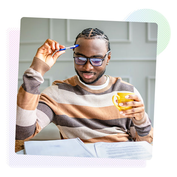 Man holding a cup, holding a pen against his head and reading notes